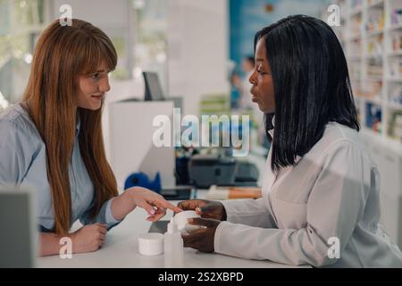 Profilansicht einer professionellen multikulturellen Drogeriemärtnerin, die mit Anti-Age-Creme in den Händen hinter der Theke steht und beim Verkauf von i erklärt Stockfoto