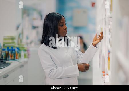 Profilansicht einer multikulturellen professionellen Drogerie, die mit einer Flasche mit Flüssigkeit in den Händen steht und das Produktetikett liest. Seitenansicht der verschiedenen p Stockfoto