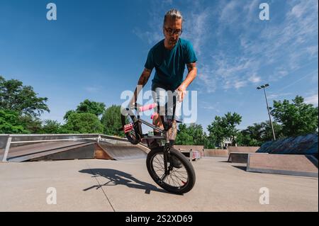 Ein Urban-Typ mittleren Alters mit Tattoos macht Tricks und Stunts auf seinem bmx in einem Skatepark und übt einen Extremsport aus. Eine alte tätowierte Ma Stockfoto