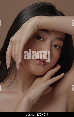 portrait of asian woman with a clean healthy skin and holding beautiful hands near her face over beige background, vertical close up photo Stockfoto