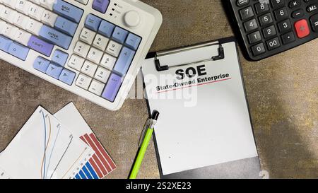 Konzept der SOE – staatseigenes Unternehmen schreibt auf Unterlagen, die auf Holztisch isoliert sind. Stockfoto