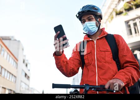 Telefon, Fahrrad und Lieferer mit Maske in der Stadt für E-Commerce, Kurier oder Transportservice. Technologie, Fahrrad und männlicher Frachtarbeiter mit Handy Stockfoto