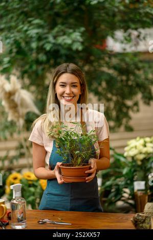 Floristin, die in einem Blumenladen arbeitet und sich um eine Pflanze kümmert, während sie neben dem Theken steht, umgeben von Blumen und Pflanzen in einem Blumenladen Stockfoto