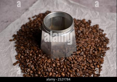 Verstreute frische aromatische Kaffeebohnen um die geysire Kaffeemaschine Mokafaschine. Heller Hintergrund. Vorbereitung zur Zubereitung von Kaffee Stockfoto