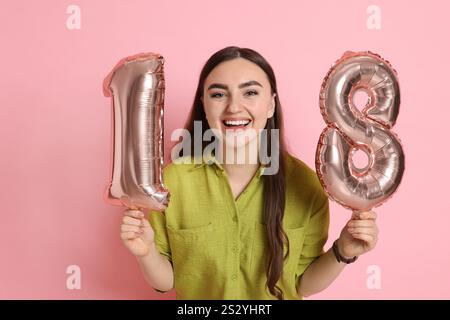 Coming of Age Party - 18. Geburtstag. Glückliche junge Frau mit zahlenförmigen Ballons auf rosa Hintergrund Stockfoto