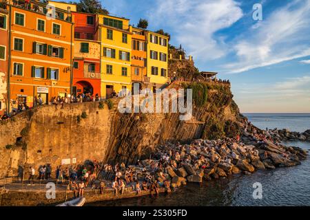 Menschenmassen versammeln sich, um den Sonnenuntergang am Hafen von Riomaggiore im Nationalpark Cinque Terre in der Region Ligurien im Nordwesten Italiens zu beobachten Stockfoto