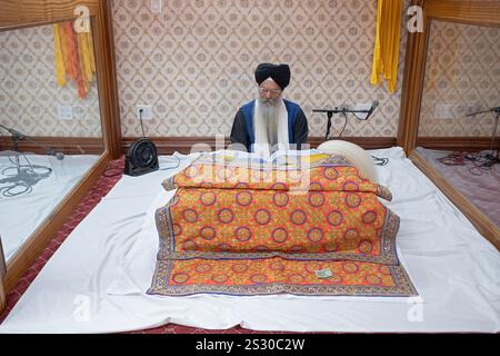 Ein Sikh-Priester liest aus dem heiligen Buch Guru Granth Sahib in einer Glaskabine in einem Tempel in Queens, New York. Stockfoto