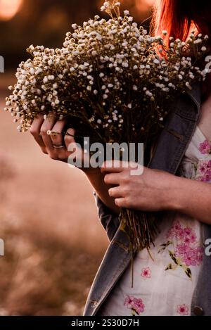 Nahaufnahme der Hände eines Mädchens, das sanft einen Strauß frischer Gänseblümchen hält. Ein wunderschöner Sommermoment, der die Einfachheit und Eleganz der Natur einfängt Stockfoto