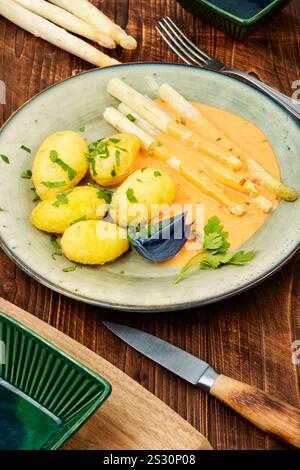 Veganes Essen, neue gekochte Kartoffeln und weißer Spargel auf rustikalem Holztisch. Stockfoto