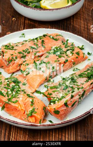 Frische Lachsfischsteaks in grüner Knoblauchmarinade zum Backen auf dem rustikalen Tisch. Stockfoto