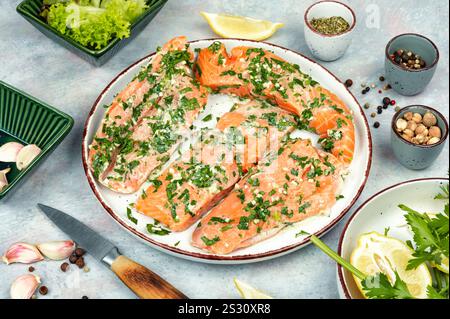 Frischer roher Lachs oder Forellenfilet in Knoblauchkräutern mariniert auf der weißen Platte. Keto-Rezept. Gravlax. Stockfoto