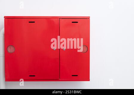 Ein hellroter Metallschrank ist auf einem weißen Wandhintergrund isoliert. Der Schrank hat zwei Türen und ist mit einem Schloss gesichert. Es gibt eine runde Inspektion h Stockfoto