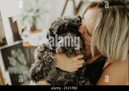 Liebe, kuschelt und eine Frau küsst ihren Hund in einem Studio oder einer Werkstatt für kreative Malerei und Kunst. Umarmung, Welpe und Maler mit einer weiblichen Tierbesitzerin Stockfoto