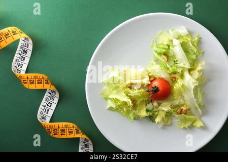 Ernährung und Gesundheit und Diätkonzept mit Detail des herzförmigen Salats mit Salat Tomate und Nüssen auf weißer Platte isoliert auf grünem Hintergrund mit Stockfoto