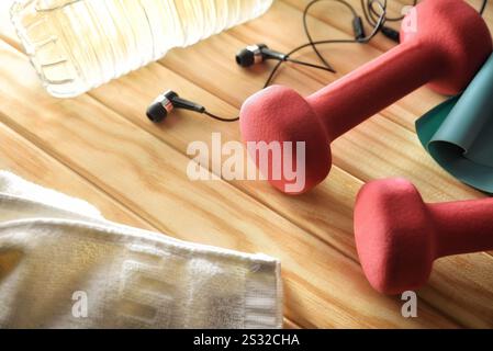 Frau Sport Training Routine Konzept und Unterhaltung mit rosa Kurzhanteln auf Holzlatten mit Ohrhörern Wasserflasche und Handtuch. Erhöhte Aussicht. Stockfoto