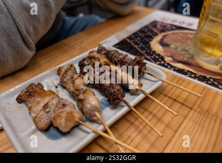 Ein wunderschön angeordneter Teller mit köstlichen Fleischspießen, der einladend auf einem Holztisch neben einem erfrischenden Glas Bier sitzt Stockfoto
