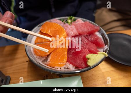 Man kann sehen, wie man eine Schüssel mit köstlichem Sushi genießt, während man die verschiedenen Stücke geschickt mit Stäbchen aufnimmt Stockfoto