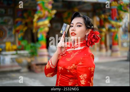 Porträt Asiatische schöne Frau trägt einen Cheongsam lächelnd und posiert Kreditkarte am Schrein am chinesischen Neujahr, Kopierraum Stockfoto