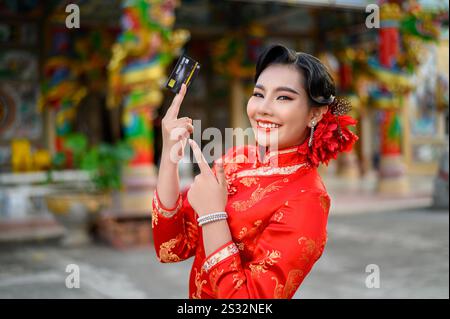 Porträt Asiatische schöne Frau trägt einen Cheongsam lächelnd und posiert Kreditkarte am Schrein am chinesischen Neujahr, Kopierraum Stockfoto