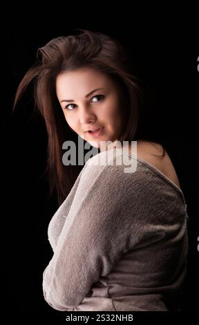 Eine junge Frau zeigt ihr fließendes Haar, während sie sich leicht zur Seite dreht und ein weiches, lässiges Oberteil trägt. Der dunkle Hintergrund verstärkt ihre Gesichtszüge Stockfoto