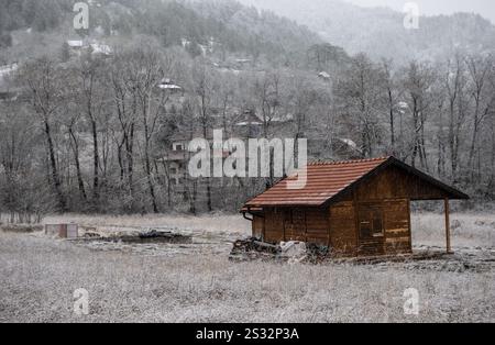 Eine malerische, kleine Holzhütte liegt friedlich inmitten eines riesigen, verschneiten Feldes, umgeben von der ruhigen Schönheit des Winters Stockfoto