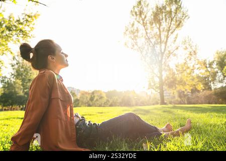 Stadtfrau, die auf dem grünen Gras im Stadtpark sitzt und sich nach der Arbeit entspannt. Work and Life Balance, psychische Gesundheit und Erholung. Stockfoto