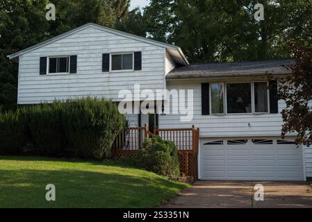 Ein zweistöckiges Haus mit abblätternder Farbe auf dem Aluminiumgleis und bewachsenen Büschen davor Stockfoto