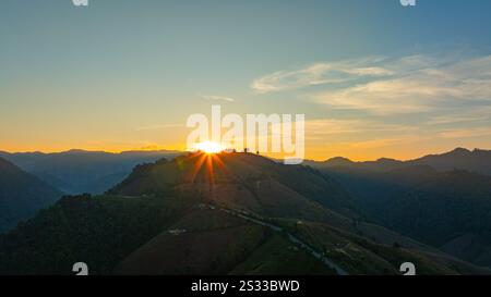 Der Blick aus der Vogelperspektive auf den ruhigen Sonnenuntergang wirft ein goldenes Leuchten über sanfte Hügel und weit entfernte Berggipfel und schafft eine friedliche und stimmungsvolle Landschaft mit Lagen Stockfoto