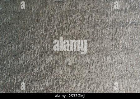 Glänzendes reflektierendes Material mit zerknitterter Aluminiumbeschichtung, versilberte Struktur der temperaturbehaltenden Verpackung, ungleichmäßig grau glänzende Oberfläche Stockfoto