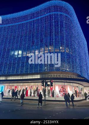 Die Fassade des Kaufhauses Peter Jones (ein John Lewis-Geschäft) ist abends mit Weihnachtslichtern dekoriert. Mit Leuten, die draußen laufen. Stockfoto
