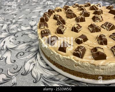 No-Bake Karamell Cheesecake mit Schokoladenbelag auf dekorativer Tischdecke, Nahperspektive Stockfoto