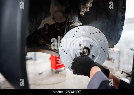Ein Mechaniker baut eine neue Bremsscheibe in einem Fahrzeug in einer Autowerkstatt ein. Das Bild zeigt die Präzision und das Know-how, das in der Automobilindustrie zum Einsatz kommt Stockfoto