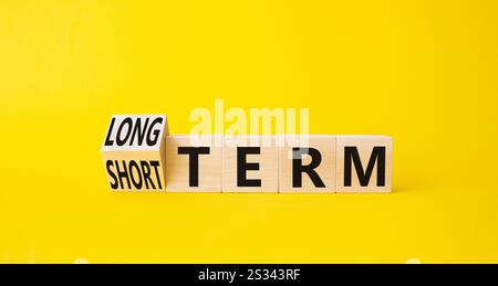 Symbol für Langzeit vs. Kurzzeit. Gedrehte Holzwürfel mit Wörtern für lange und kurze Zeit. Schöner gelber Hintergrund. Geschäftskonzept. Kopierbereich. Stockfoto