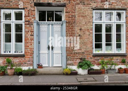Grauweiße alte Haustür und Gitterfenster und Pflanztöpfe am alten Haus Stockfoto