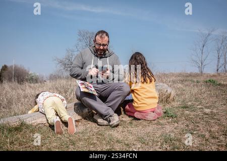 Vater, der an einem sonnigen Tag am Baum sitzt, mit zwei Kindern neben ihm Stockfoto