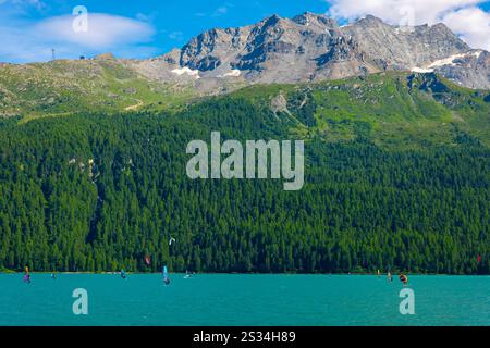 Windsurfen und Wingsurfen auf dem Alpensee Silvaplana an einem sonnigen Sommertag mit Berg in Silvaplana, Maloja, Graubünden, Schweiz. Stockfoto