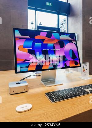 Paris, Frankreich - 10. Dezember 2024: Ein schlankes Mac Mini-Setup mit Studio-Display mit brillanter Grafik, Tastatur und Werbeletiketten, präsentiert auf einem Holztisch in einem modernen Verkaufsraum. Stockfoto