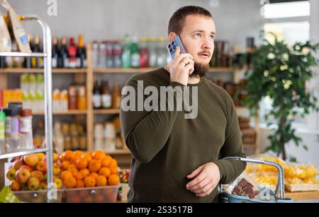 Einkaufen im Supermarkt - Mann mit Einkaufswagen spricht mit Handy im Supermarkt Stockfoto