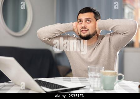 Mann, der die Ohren mit Händen bedeckt, wegen lautem Lärm in der Nachbarwohnung Stockfoto