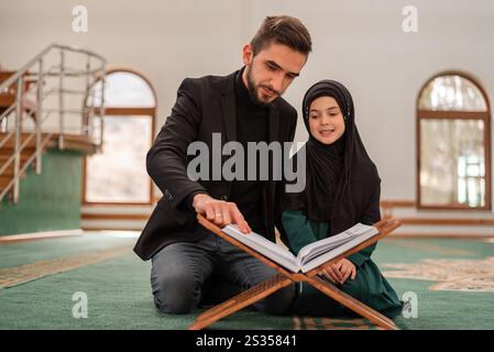 Ein muslimischer Lehrer, der einem Mädchen beibringt, ein heiliges Buch Quran in der Moschee zu lesen. Islamische Menschen beten in der masjid. Stockfoto