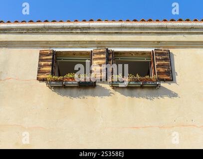 Blumentöpfe schmücken die Wände und Holzfenster des cremefarbenen Hauses. Farbenfrohe Architektur in Venedig, Italien Stockfoto