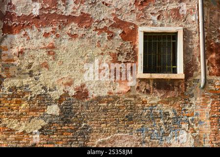 Weißes Fenster an der orangen alten Hauswand Risse in Beton sichtbare rote Ziegelsteine in Venedig, Italien. Stockfoto