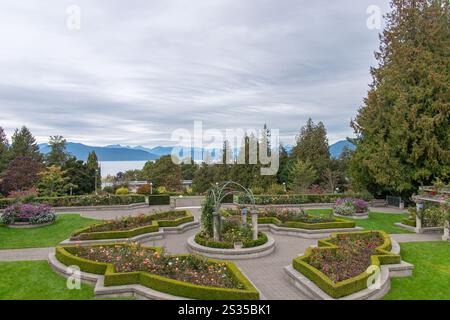 Der UBC Rose Garden bietet lebendige Blumenbeete, gepflegte Hecken und einen Blick auf das Meer mit weit entfernten Bergen unter einem bewölkten Himmel. Stockfoto