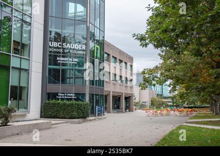 Moderner Außenblick auf die UBC Sauder School of Business, mit großen Glasfenstern, Sitzgelegenheiten im Freien und umliegenden Grünflächen auf dem Campus. Stockfoto