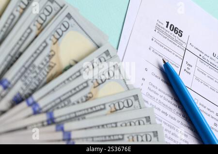 1065 Steuerformular liegt in der Nähe von Hundert-euro-Scheine und blauen Stift auf einem hellblauen Hintergrund. Uns parentship Einkommen. Stockfoto