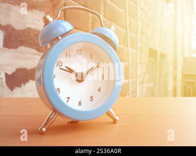 Kleiner blauer Wecker auf rotem Backsteinmauer Hintergrund in der Morgensonne. Stockfoto