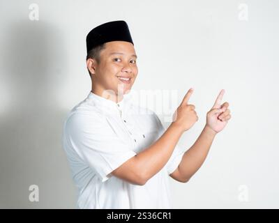 Porträt eines muslimisch-asiatischen Mannes mit weißem Hemd und schwarzer Kappe, der mit dem Finger auf freien Platz für eine Werbung zeigt. Stockfoto