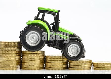 Die Landwirte in der Landwirtschaft müssen mit steigenden Kosten rechnen. Höhere Preise für Futtermittel, Düngemittel und Pflanzen. Traktor mit Münzen Stockfoto