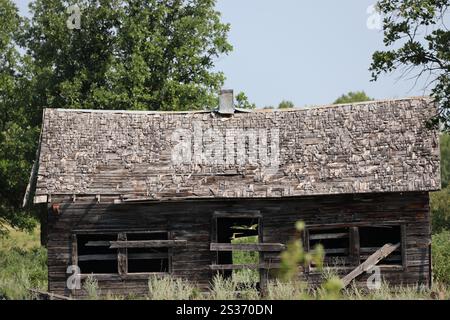 Verlassenes Bauernhaus mit verrottetem Dach auf bewachsener Wiese Stockfoto