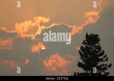 Die Sonne, die kaum durch schwere Wolken schaut, erleuchtet sie in Rot, Orange, Gelb und Gold Stockfoto